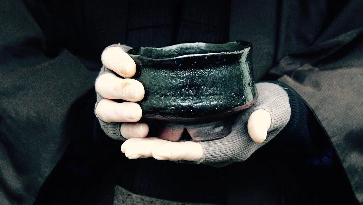 Twee handen die een zwarte matcha kom van keramiek tonen.