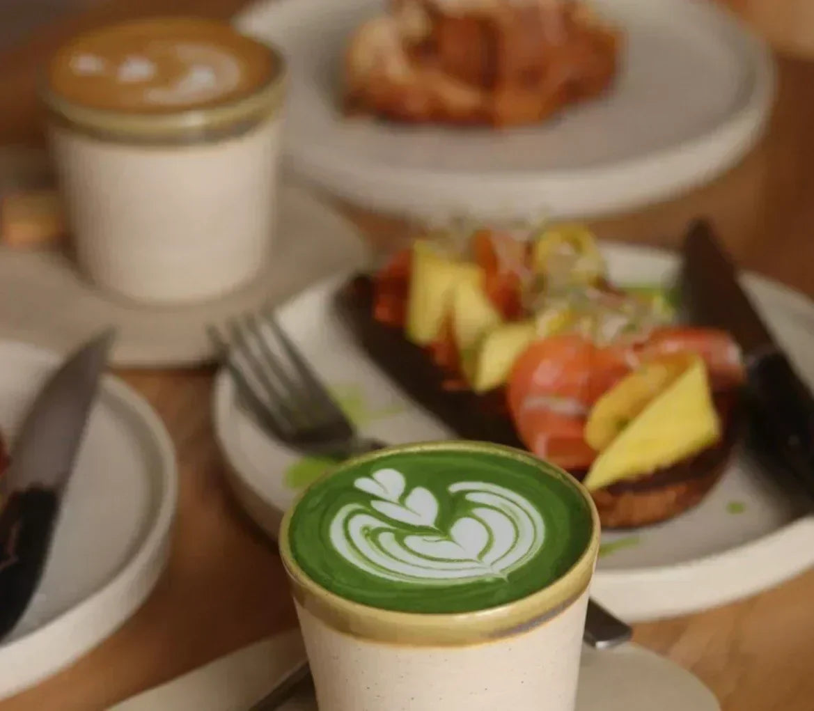 Een ontbijt met op de voorgrond een beker met matcha latte.