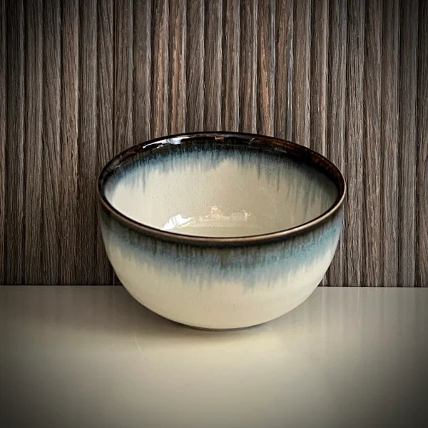 Voorkant van een lichtblauwe matcha komvan keramiek met zwarte rand.