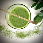 Een met matcha gevulde glazen matcha  kom  met tuit en een bamboelepel.