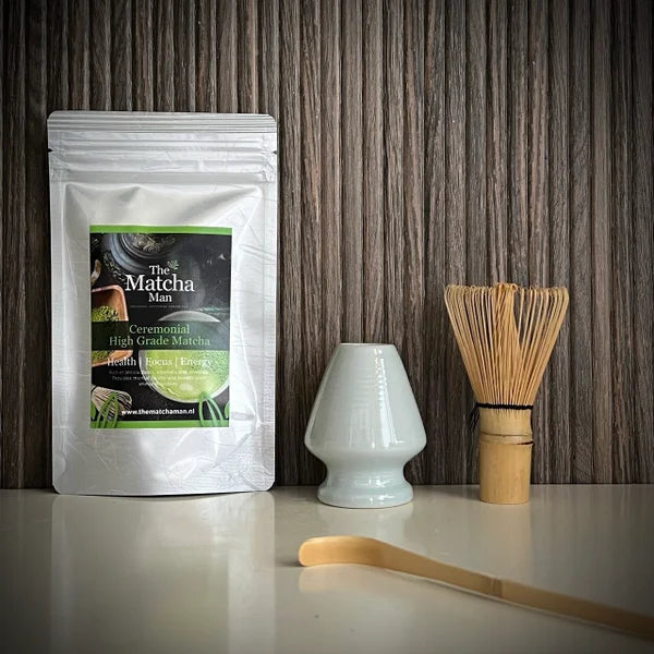 Hersluitbaar zakje Ceremonial High Grade Matcha, een kom, een lichtblauwe bamboe matchaklopper en een bamboelepel op de voorgrond.
