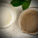 Een glas opgeschuimde melk, een glazen matcha kom met tuit, gevuld met hojicha latte.