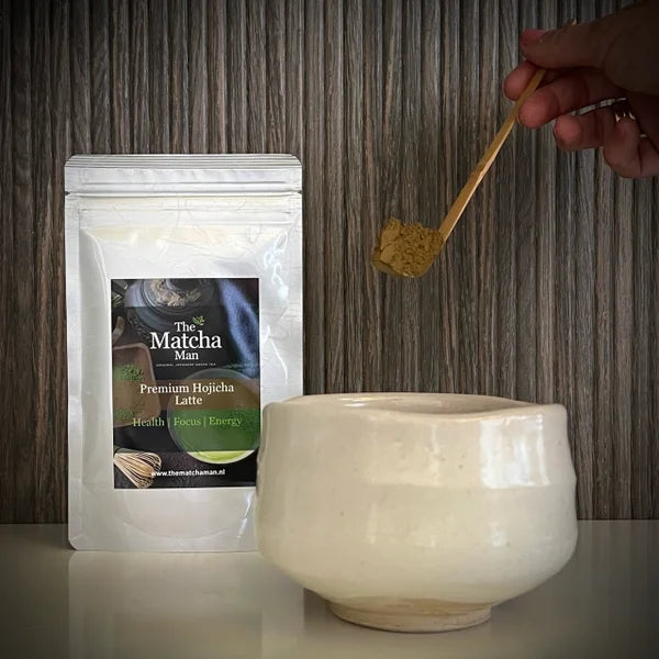 Hersluitbaar zakje 'Premium Hojicha latte' van The Matcha Man uit Japan, een witte matcha kom en een hand met een bamboelepel met hojicha.
