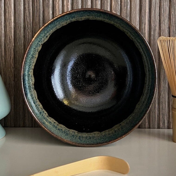 Binnenkant van een geglazuurde zwarte matcha kom van keramiek met groen-blauwe rand.