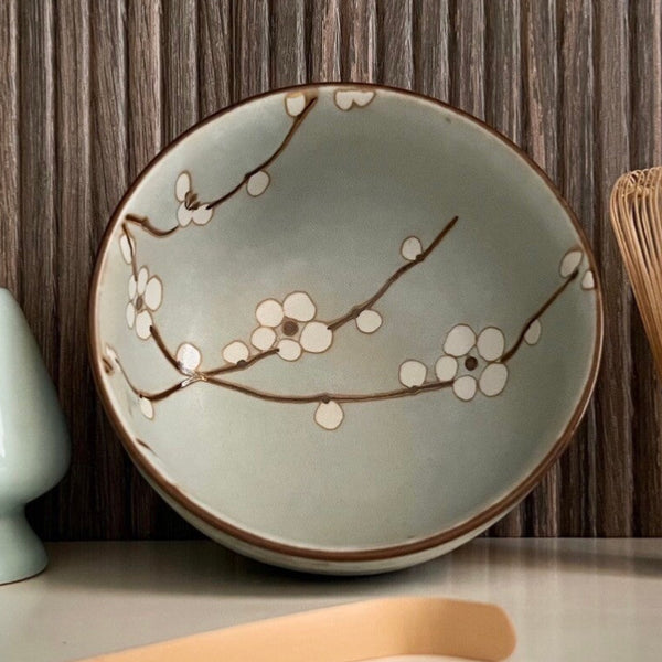 Binnenkant van een lichtgroene matcha kom van keramiek met bloesemtakken.