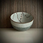 Voorkant van een lichtgroene matcha kom van keramiek met bloesemtakken met bruine rand aan de buitenkant.