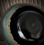 Close up van een geglazuurde zwarte matcha kom van keramiek met groen-blauwe rand.