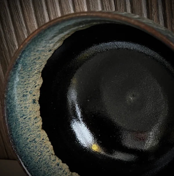 Close up van een geglazuurde zwarte matcha kom van keramiek met groen-blauwe rand.