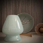 Matcha set met groene matcha kom met bloesem, inclusief bamboelepel, bamboe matcha klopper en lichtblauwe whiskhouder op voorgrond.