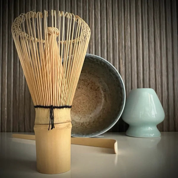 Matcha set met beige matcha kom met zachtblauwe tinten, inclusief bamboe matcha klopper, bamboelepel, lcihtblauwe whiskhouder en whisk op de voorgrond.