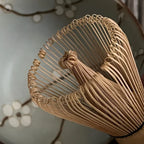 Deel van een bamboe matcha klopper met bloesemtakken op achtergond.