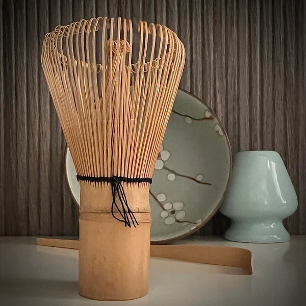 Matcha set met groene matcha kom met bloesemtakken, inclusief bamboelepel, lichtblauwe whiskhouder en bamboe matcha klopper op voorgrond.