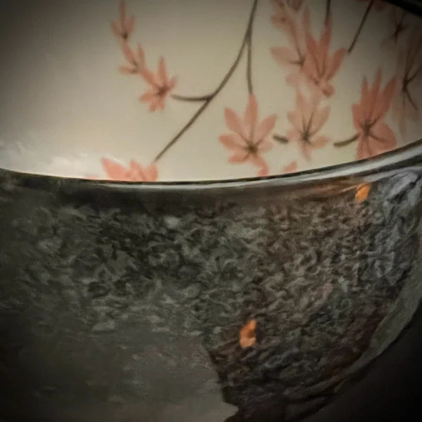 Antracietgrijze buitenkant van een matcha kom van keramiek met oudroze bloesemtakken.
