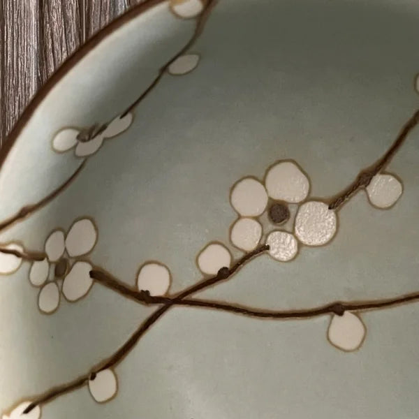 Close up van een lichtgroene matcha kom van keramiek met bloesemtakken.