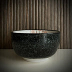 Voorzijde van een matcha kom van keramiek met oudroze bloesemtakken en antracietgrijze buitenkant.