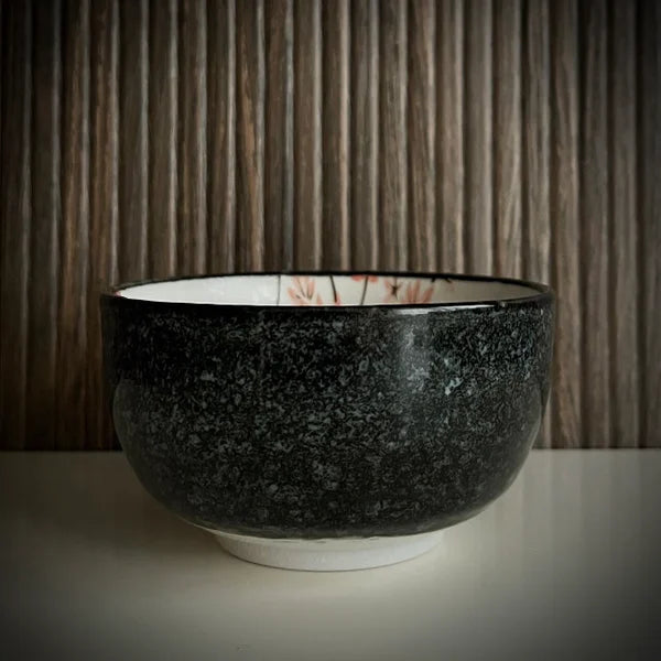 Voorzijde van een matcha kom van keramiek met oudroze bloesemtakken en antracietgrijze buitenkant.