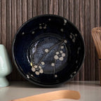Binnenkant van een donkerblauw matcha kom van keramiek met bloesemtakken.