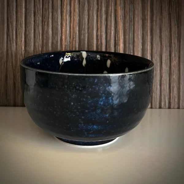 Voorkant donkerblauwe matcha kom met witte bloesemtakken.