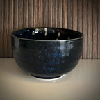 Voorzijde van een donkerblauwe matcha kom van keramiek met bloesemtakken.