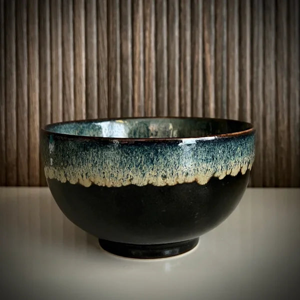 Voorzijde van een geglazuurde zwarte matcha kom van keramiek met groen-blauwe rand.