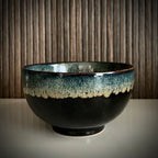 Voorzijde van een geglazuurde zwarte matcha kom van keramiek met groen-blauwe rand.