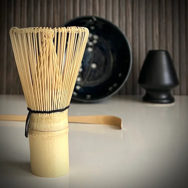 Matcha set met donkerblauwe matcha kom met bloesemtakken, inclusief bamboelepel, zwarte whiskhouder en bamboe matcha klopper op voorgrond.