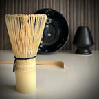 Matcha set met donkerblauwe matcha kom met bloesemtakken, inclusief bamboelepel, zwarte whiskhouder en bamboe matcha klopper op voorgrond.