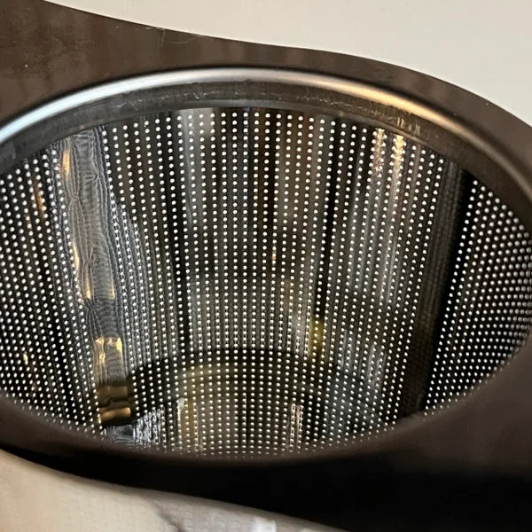 Close up van een roestvrij stalen theefilter met vleugels en roestvrij stalen lekschaaltje.