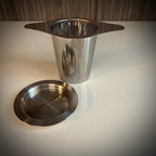 Roestvrij stalen theefilter met vleugels en roestvrijstalen lekschaaltje.