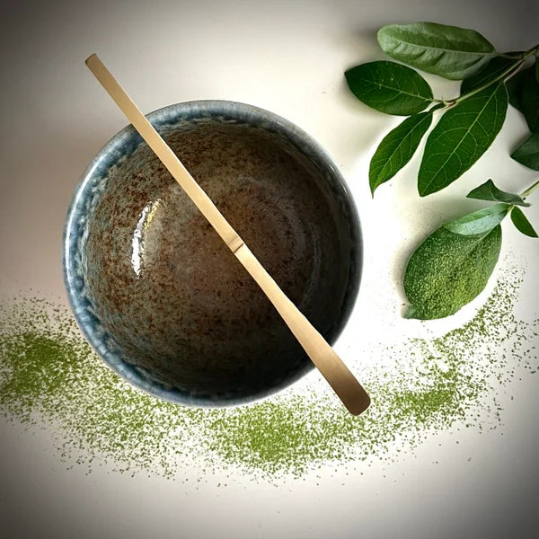 Beige matcha kom met zachtblauwe rand en een bamboelepel.