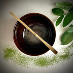 Bovenaanzicht van een bordeaux matcha kom en een bamboelepel.