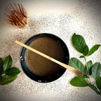 Bovenaanzicht van een donkerblauwe matcha kom van keramiek met bloesemtakken gevuld met hojicha en bamboelepel.