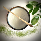 Bovenaanzicht van een lichtblauwe matcha kom van keramiek met zwarte rand en bamboelepel.