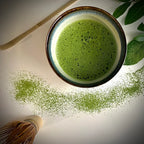 Bovenaanzicht van een lichtblauwe matcha kom van keramiek met zwarte rand gevuld met matcha en bamboelepel.