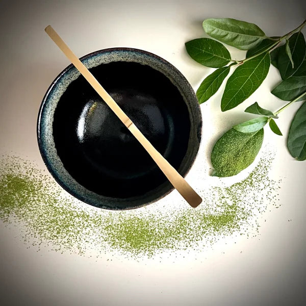 Zwarte matcha kom met groene rand  en een bamboelepel.
