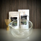 Matcha set van The Matcha Man , bestaande uit hersluitbaar zakje 'Matcha for Latte Pure' en hersluitbaar zakje 'Matcha for Latte Vanilla', een bamboe matcha klopper een glazen matcha kom op voorgrond.