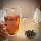 Hand met dubbelwandig theeglas en glazen theefilter met losse thee.