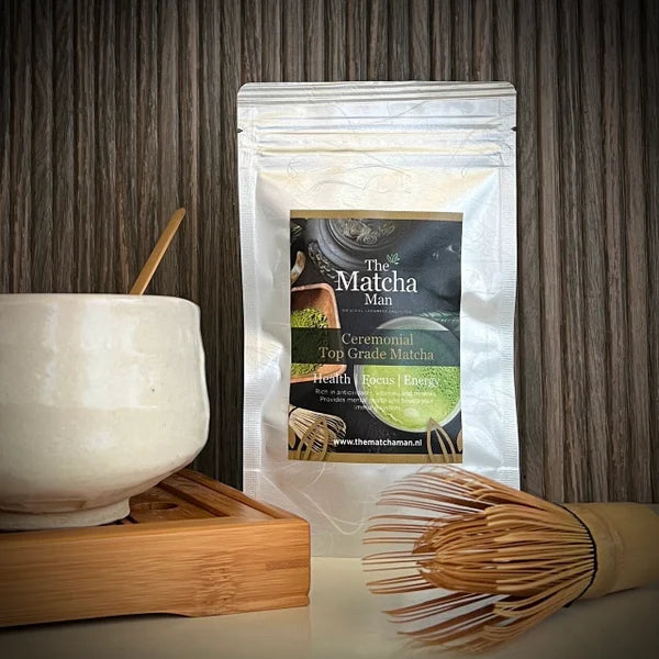 Hersluitbaar zakje 'Ceremonial Top Grade Matcha' van The Matcha Man (25 gram) , een bamboe bamboe matcha klopper en een witte matcha kom op een serveerblaaadje.